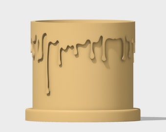 May include: A tan-colored ceramic planter with a drip design around the top edge. The planter has a wide base and a cylindrical shape.
