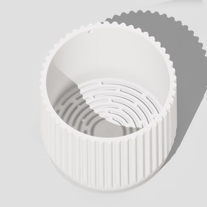 May include: White ceramic planter with a ribbed exterior and a drainage hole. The planter has a removable inner pot with a grid pattern.