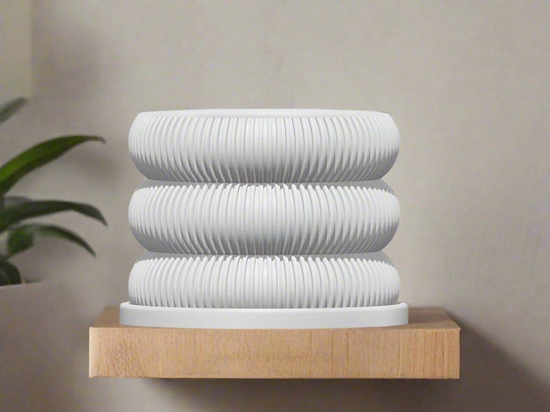 May include: A white ceramic planter with a ribbed design. The planter is stacked in three tiers and sits on a wooden shelf.