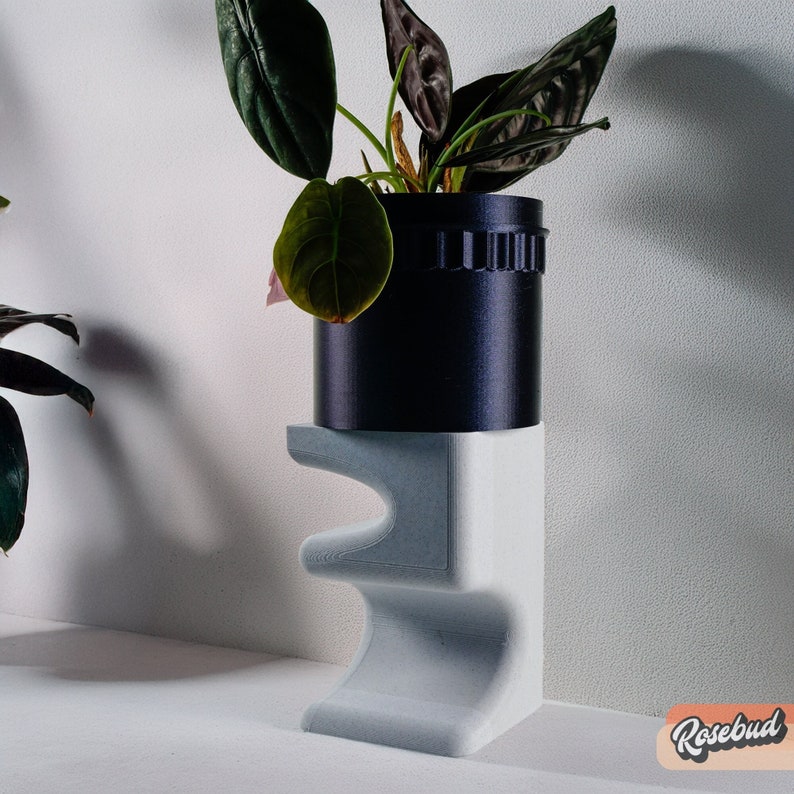 May include: A gray concrete plant stand with a black planter and a leafy green plant. The plant stand has a unique, organic shape.