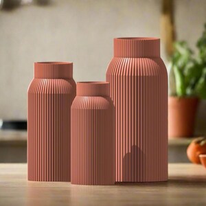 May include: Three terracotta-colored ceramic vases with a ribbed texture. The vases are arranged in a row from largest to smallest.