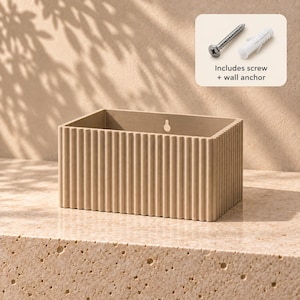 May include: A rectangular beige wall-mounted planter with a vertical ribbed texture on the exterior. The back panel features a keyhole slot for mounting. A small inset graphic shows a metal screw and a white plastic wall anchor with the text Includes screw + wall anchor.