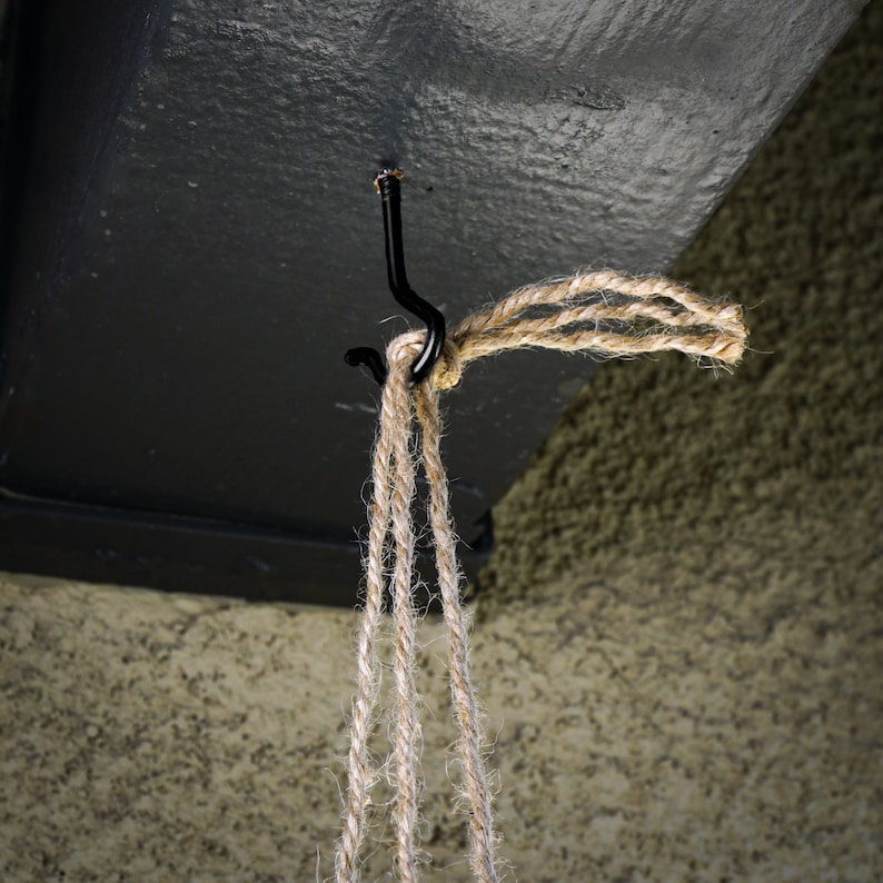 May include: A close-up of a black metal hook attached to a ceiling, with a length of natural twine hanging from it.