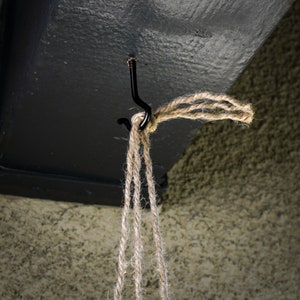 May include: A close-up of a black metal hook attached to a ceiling, with a length of natural twine hanging from it.