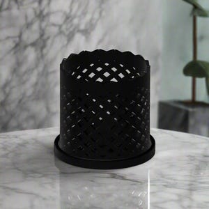 Puede incluir: Candelero de metal negro con un diseño de rejilla geométrica. El candelero tiene una base redonda y una parte superior festoneada.