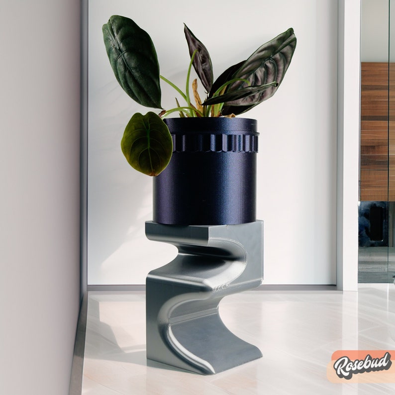 May include: A dark blue ceramic planter with a plant with dark green leaves sits on a gray, abstract, 3D printed stand. The stand has a unique, wavy design.