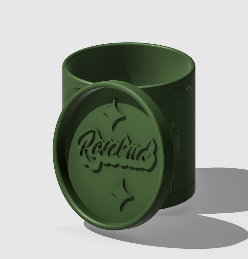 Op de afbeelding: Een groene cilindrische container met een deksel. Het deksel heeft het woord "Roadbud" erop gegraveerd. De container heeft een ontwerp van cactussen en sterren.
