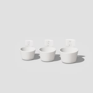 May include: Three white ceramic wall-mounted planters with a simple design. Each planter has two small holes on the back for hanging.