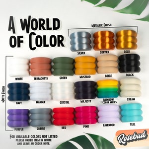 May include: A color chart showing 18 different colors of silicone rings. The colors are arranged in three rows of six. The colors are: white, terracotta, green, mustard, beige, black, navy, marble, crystal, majesty, rainbow, cream, purple, greige, red, pink, lavender, and teal. The chart also includes the words "Matte Finish" and "Metallic Finish".