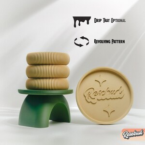 May include: A set of three beige, stacked, round, ceramic candle holders with a ribbed texture. The candle holders are on a green, arched stand. A beige, round, ceramic coaster with the word "Rosebud" in a stylized font and two stars is also shown. The text "Drip Tray Optional" and "Revolving Pattern" are shown in black text.
