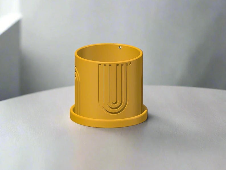 May include: A yellow ceramic planter with a geometric design. The planter has a wide base and a cylindrical shape.
