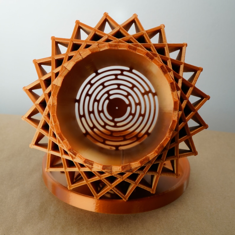 May include: A copper-coloured, geometric, star-shaped object with a circular opening in the centre. The opening has a concentric circle pattern.