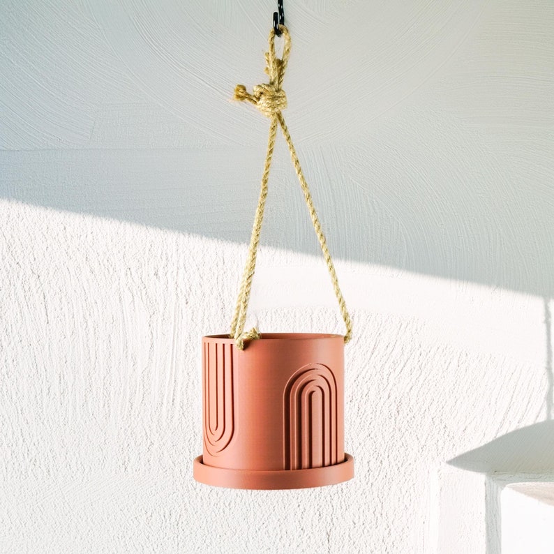 May include: A terracotta hanging planter with a geometric design. The planter is suspended from a natural rope.