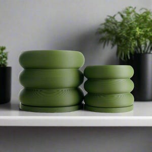 May include: Two green ceramic planters with a ribbed texture. The larger planter is taller and wider than the smaller planter.