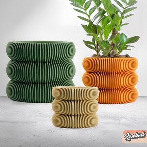 May include: Three plant pots in different sizes and colours. The largest pot is green, the medium pot is orange, and the smallest pot is beige. All three pots have a ribbed design.