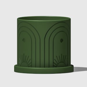 May include: A dark green ceramic planter with a geometric design featuring arches and sunbursts. The planter has a drainage hole and a matching saucer.
