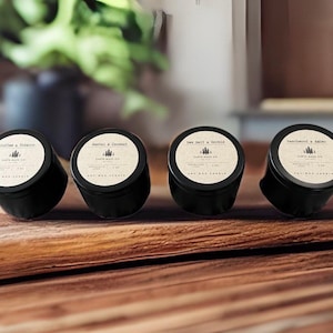 May include: Four black soy wax candles with white labels. The labels read "Coffee & Tobacco", "Santal & Coconut", "Sea Salt & Orchid", and "Beachwood & Amber". Each candle is in a small, round tin.