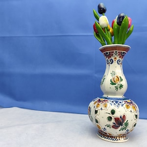 Può includere: Un vaso di ceramica bianca con motivi floreali blu e arancioni, decorato con un mazzo di tulipani di legno di vari colori, tra cui rosso, bianco e nero.