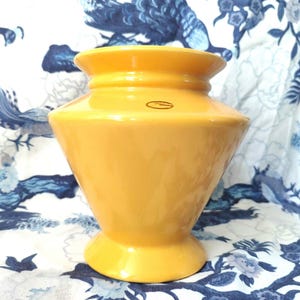 May include: A yellow ceramic vase with a wide base and a narrow neck. The vase has a smooth, glossy finish and a subtle, rounded shape.