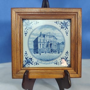 May include: A framed blue and white Delft tile with a depiction of a building and the text "Scheielandschuis".