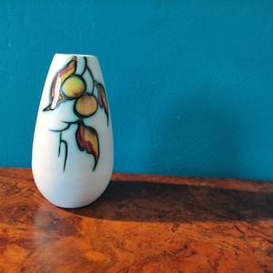 May include: A white ceramic vase with a teardrop shape and a floral design in shades of yellow, red, and green.