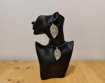 May include: A silver leaf necklace and matching earrings. The necklace and earrings are on a black mannequin bust.