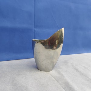 May include: A silver metal vase with a unique, curved design. The vase is smooth and reflective, with a modern aesthetic.