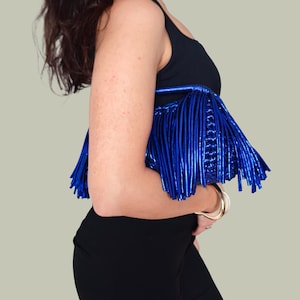 May include: A black top with a metallic blue fringe detail. The fringe is made of vertical, shiny strips. The top is paired with black pants and gold bracelets.