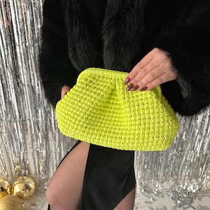 May include: A bright neon green crocheted clutch bag. The bag has a gathered, puffy design and is made of a thick, textured yarn.