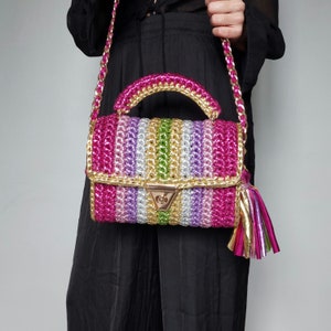 May include: A multi-colored crocheted handbag with a gold chain strap and a gold tassel. The bag is made of pink, purple, green, and gold yarn.