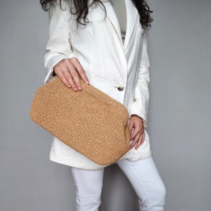 Könnte beinhalten: Eine Frau hält eine braune gehäkelte Clutch. Die Clutch ist aus einem gewebten Material und hat eine rechteckige Form.