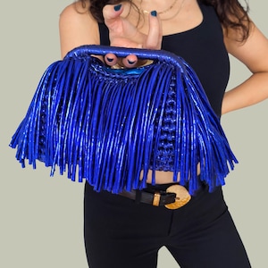 May include: A vibrant blue handbag with a fringe design. The bag features a woven base and a structured handle. The fringe detail adds a unique texture and visual interest to the accessory. The bag is a bold fashion statement.