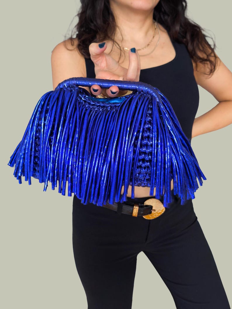 May include: A vibrant blue handbag with a fringe design. The bag features a woven base and a structured handle. The fringe detail adds a unique texture and visual interest to the accessory. The bag is a bold fashion statement.