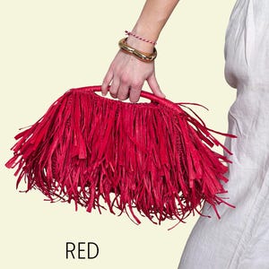 May include: A bright red raffia handbag with a fringed design. The bag is held by a person wearing a gold bracelet and a red and white string bracelet. The word "RED" is printed below the bag.