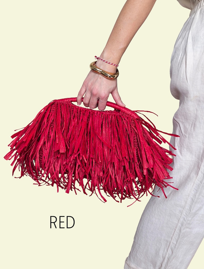 May include: A bright red raffia handbag with a fringed design. The bag is held by a person wearing a gold bracelet and a red and white string bracelet. The word "RED" is printed below the bag.