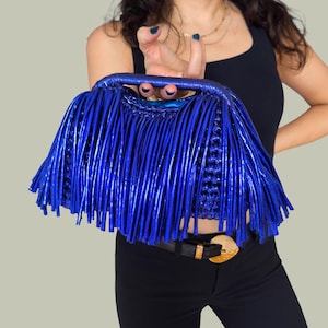 May include: A vibrant blue handbag with a fringe design. The bag features a woven top handle and a body covered in long, vertical fringe. The color is a bright, electric blue, creating a bold and stylish accessory.