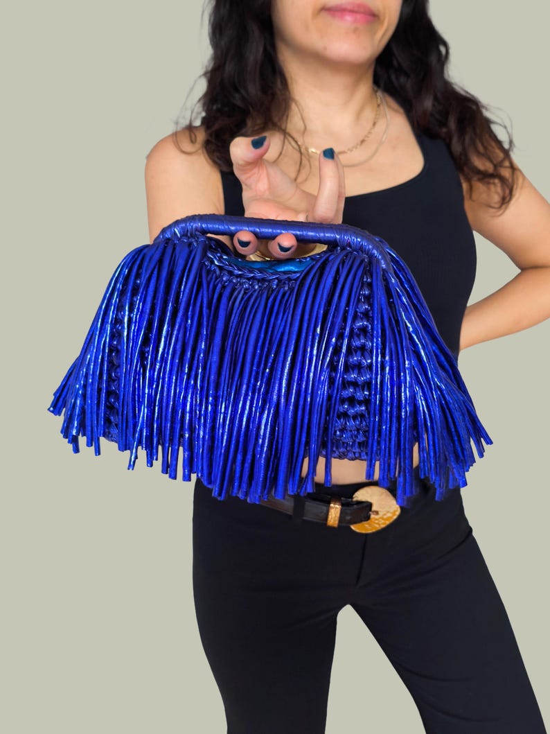 May include: A vibrant blue handbag with a fringe design. The bag features a woven top handle and a body covered in long, vertical fringe. The color is a bright, electric blue, creating a bold and stylish accessory.