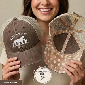 Op de afbeelding: Twee chocoladebruine truckerpetten met mesh-achterkanten. E&eacute;n pet heeft de tekst "Dutton Ranch" met een paardenafbeelding en "ESTD. 2006". De andere pet heeft een gevlekt patroon aan de onderkant. De petten maken deel uit van een borduurontwerp.