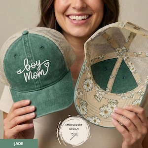 Op de afbeelding: Jade groene truckerpet met de geborduurde tekst "boy mom" in witte letters. De pet heeft een mesh achterkant en een bloemenpatroon aan de binnenkant. Een modieus accessoire.