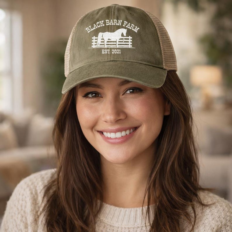Op de afbeelding: Olijfgroene baseballcap met een mesh achterkant. De cap heeft de tekst "BLACK BARN FARM" boven een witte paardenafbeelding en de tekst "EST. 2021". De cap wordt door een persoon gedragen.