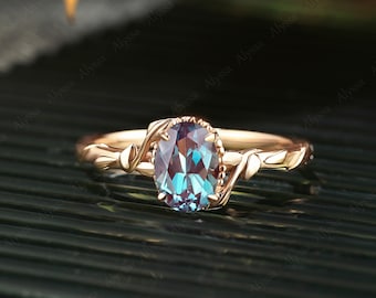 Puede incluir: Un anillo de compromiso de oro rosa con una piedra preciosa de alexandrita ovalada azul y verde engastada en un diseño de vid enredada.