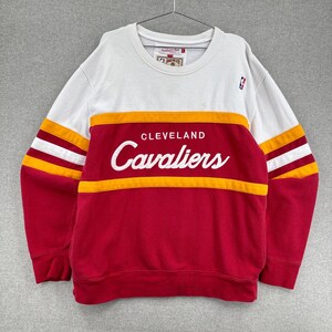 May include: A white, red, and yellow Cleveland Cavaliers sweatshirt. The sweatshirt has a white upper section, red lower section, and yellow and white stripes on the sleeves. The team name "Cavaliers" is displayed in white script across the chest.
