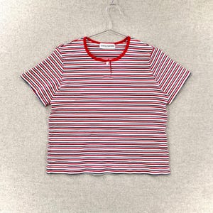 May include: A short-sleeved striped shirt with red, white, and navy blue horizontal stripes. The shirt has a red collar and trim, and a single button closure. The brand name "cathy daniels" is printed on the collar.