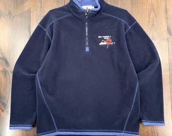 Könnte beinhalten: Ein marineblauer Fleece-Pullover mit einem Viertel-Reißverschluss und einem hellblauen Kragen und Bündchen. Der Pullover hat eine kleine Grafik auf der Brust mit dem Text "Most Treedment in Canada".