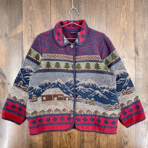 May include: A patterned button-down jacket with a mountain and cabin design. The jacket features a red, blue, green, and grey colour scheme. The collar and cuffs are red, and the jacket has a round collar.