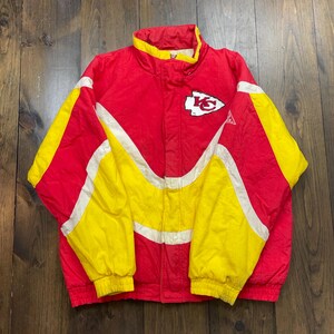 May include: A vintage Kansas City Chiefs jacket in red, white and yellow with a team logo on the front. The jacket has a zip fastening and a stand-up collar.