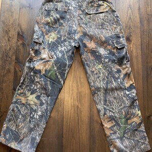 May include: Camouflage cargo pants with a brown, green, and white pattern. The pants have two large cargo pockets on the sides and a belt loop.