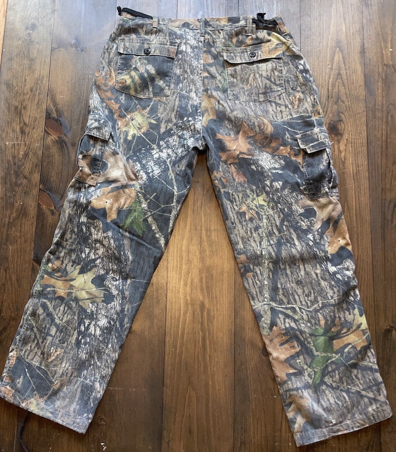 May include: Camouflage cargo pants with a brown, green, and white pattern. The pants have two large cargo pockets on the sides and a belt loop.