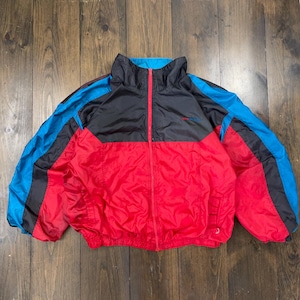 Peut inclure: Veste coupe-vent vintage avec un design color block. La veste présente une section inférieure rouge, une section supérieure noire et des accents bleus sur les manches. Elle a une fermeture éclair complète et un col montant.