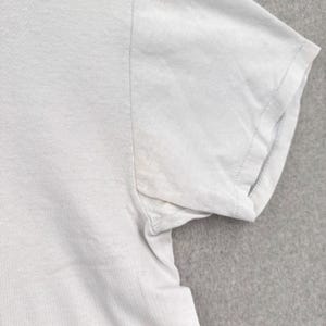 May include: Close-up of a light gray t-shirt sleeve. The sleeve is short and has a stitched hem. The fabric appears to be a soft, lightweight material. The shirt is plain and without any visible graphics or patterns.
